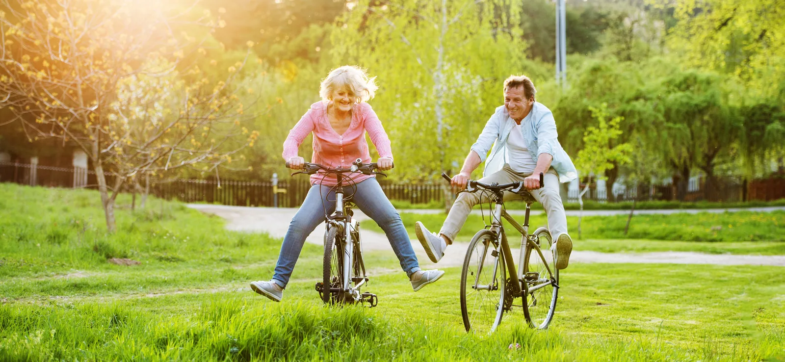 A couple riding bikes through a sunlit park, laughing with their feet off the pedals